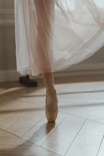 How to prepare for your first pointe shoe fitting. Image showing a foot en pointe, with a single leg in a long sheer dqnce skirt.