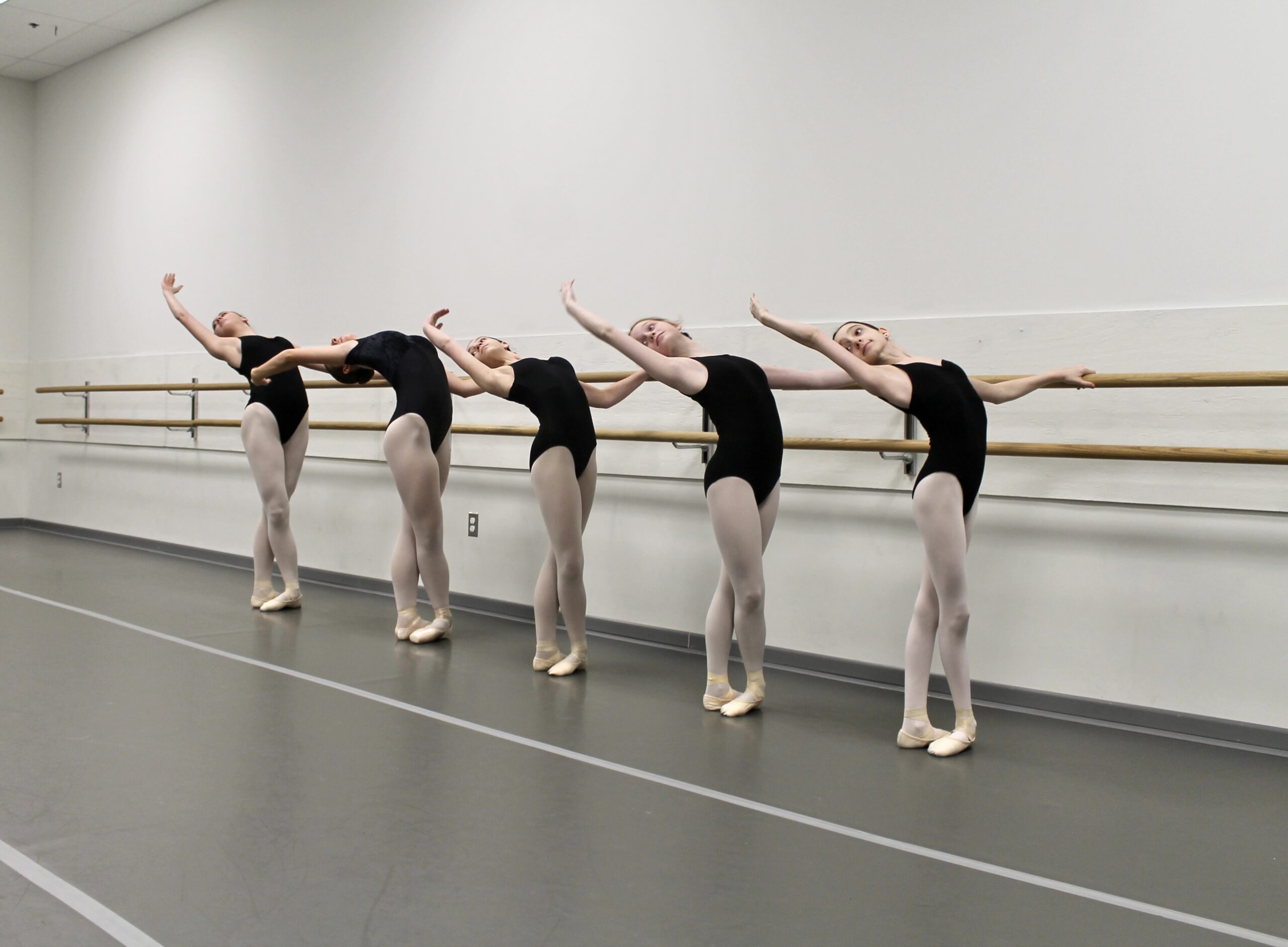 Five VBC dancers perform port de bras at barre.